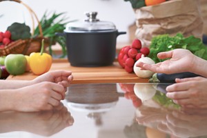 Close-up of four human hands are gesticulate over a table in the kitchen. Friends having fun while choosing menu or making online shopping. So much ideas for tasty cooking. Vegetarian, healthy meal and friendship concept